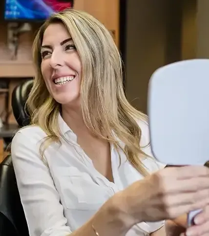 Dental patient looking at her smile in a mirror during cosmetic dentistry consultation