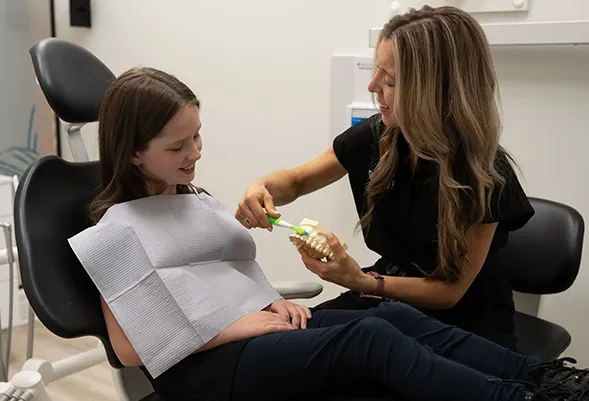 Dental Hygienist demonstrating to young patient how to brush using a dental model